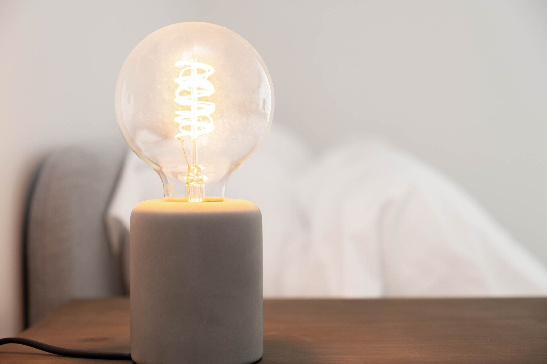 Una lampadina in vetro trasparente con filamento a spirale su un supporto in legno chiaro, posata su una superficie di legno.