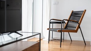 A modern living room with a wooden floor, a glass coffee table, a black and wooden chair, and a television.
