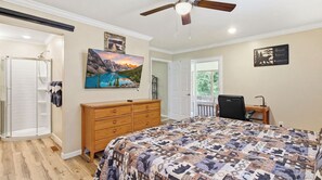 A bedroom with a bed, a wooden dresser, a desk with a chair, a ceiling fan, and a painting of a mountain landscape. - Trevor’s Riverfront Retreat w Hot Tub & Kayaks (Pigeon Forge)