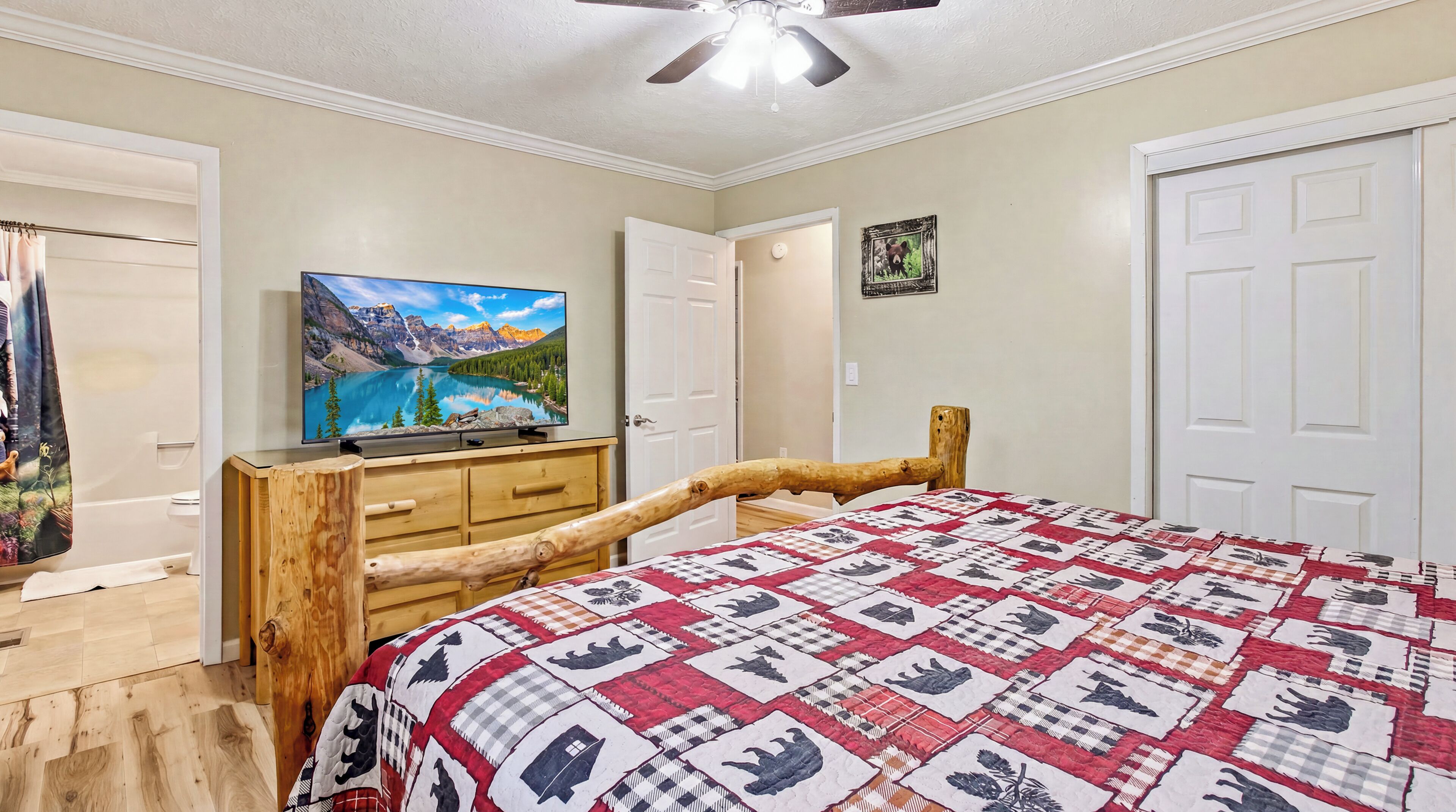 A bedroom with a wooden bed frame, a television on a wooden dresser, and a quilt with animal patterns.