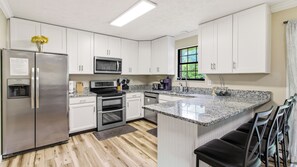 A modern kitchen with white cabinets, stainless steel appliances, and a granite countertop. - Trevor’s Riverfront Retreat w Hot Tub & Kayaks (Pigeon Forge)