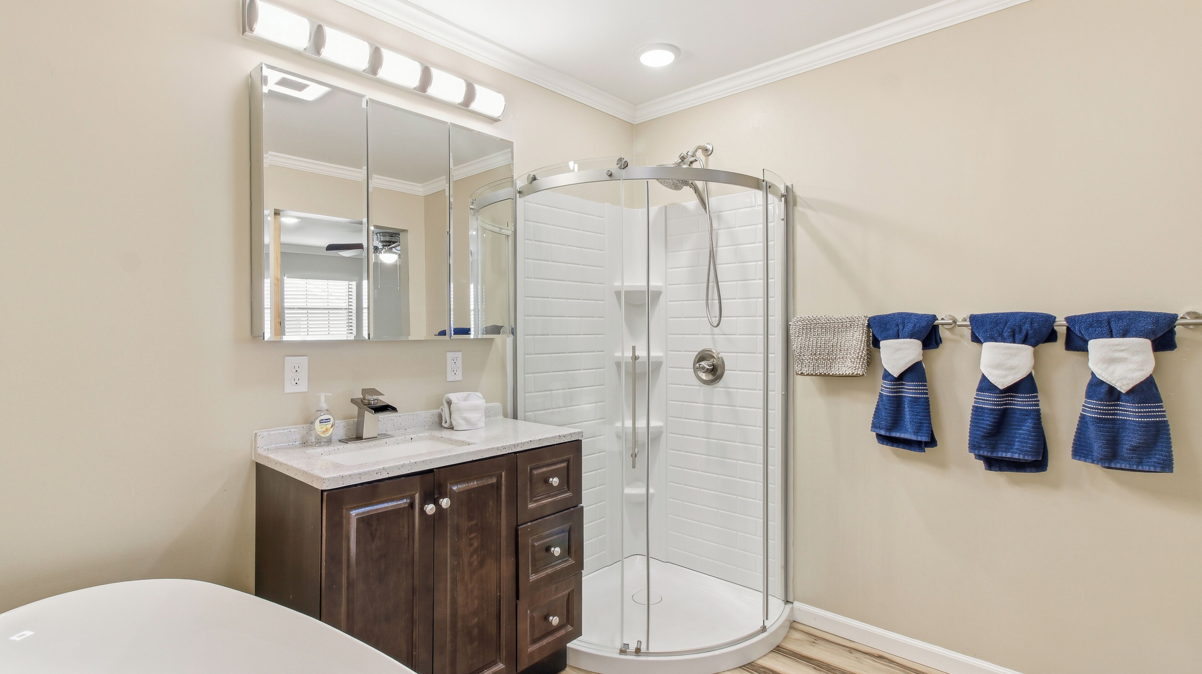 A bathroom with a glass shower enclosure, a vanity with a mirror, and towels hanging on the wall.