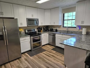 A modern kitchen with white cabinets, stainless steel appliances, and a granite countertop.