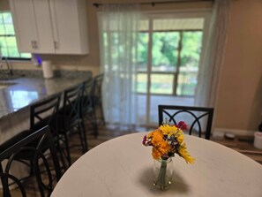 A kitchen with a white table, chairs, and a vase with flowers.