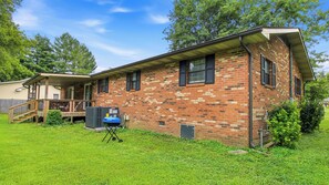 A brick house with a covered porch, a visible air conditioning unit, and a small deck. - Trevor’s Riverfront Retreat w Hot Tub & Kayaks (Pigeon Forge)