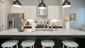 Una cocina moderna con una isla grande, electrodomésticos de acero inoxidable e iluminación colgante.