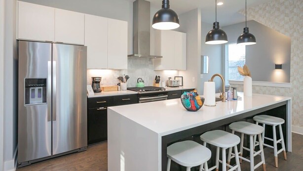 Een moderne keuken met een roestvrijstalen koelkast, een centraal kookeiland met krukken, hanglampen en een groot raam.