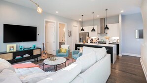 Een moderne woonkamer met een bank, een salontafel en een televisie. Er is een keuken met kastjes en een eettafel.