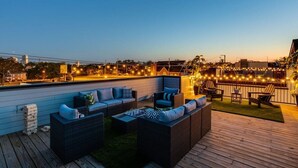 Een dak terras met buiten zitplaatsen, lichtjes en een uitzicht op de stad in de schemering.