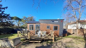 A small wooden cabin with a deck and two chairs, surrounded by a fenced yard and trees. - House with garden 2 bedrooms Soulac Sur Mer 500m from the beach (Soulac-sur-Mer)