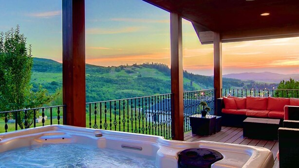 A hot tub on a wooden deck with a scenic view of hills and a sunset.