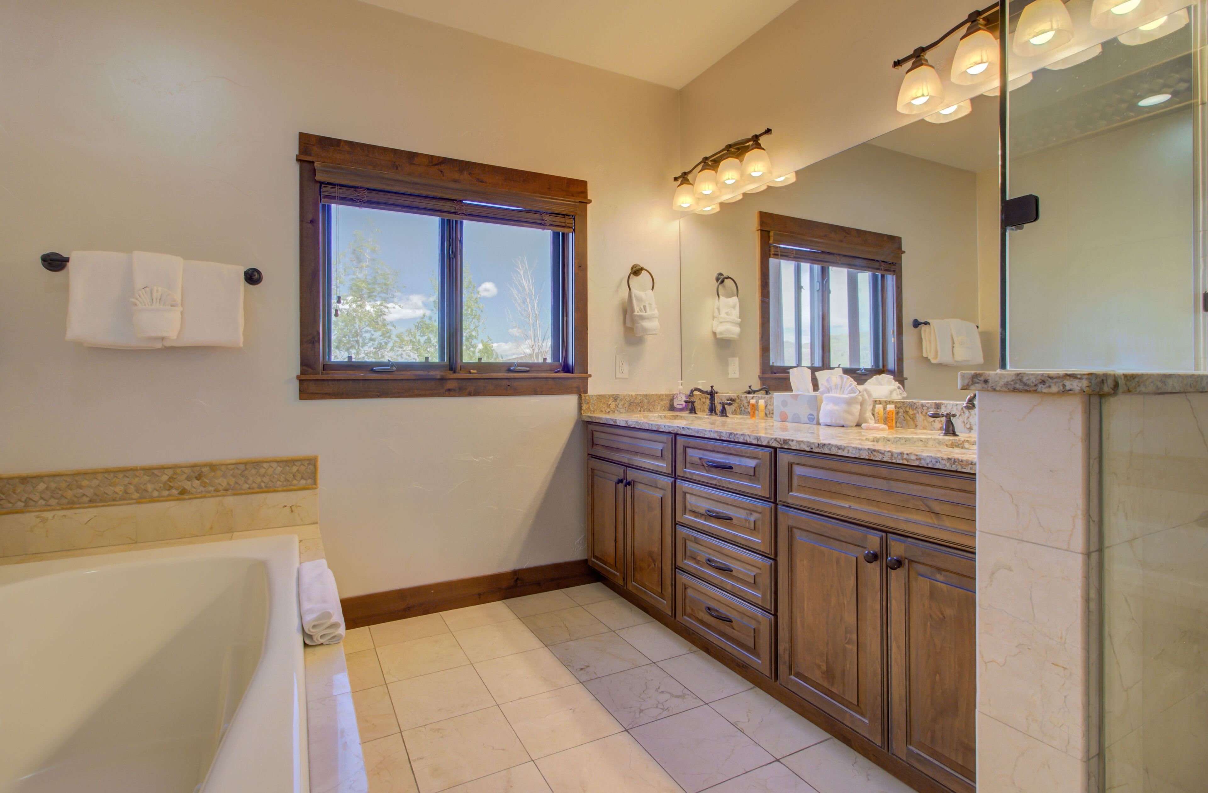 A modern bathroom with a bathtub, wooden cabinets, a large mirror, and a window.