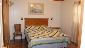 Un dormitorio con cabecera de madera, colcha acolchada, una silla, una mesita de noche y un cuadro en la pared.