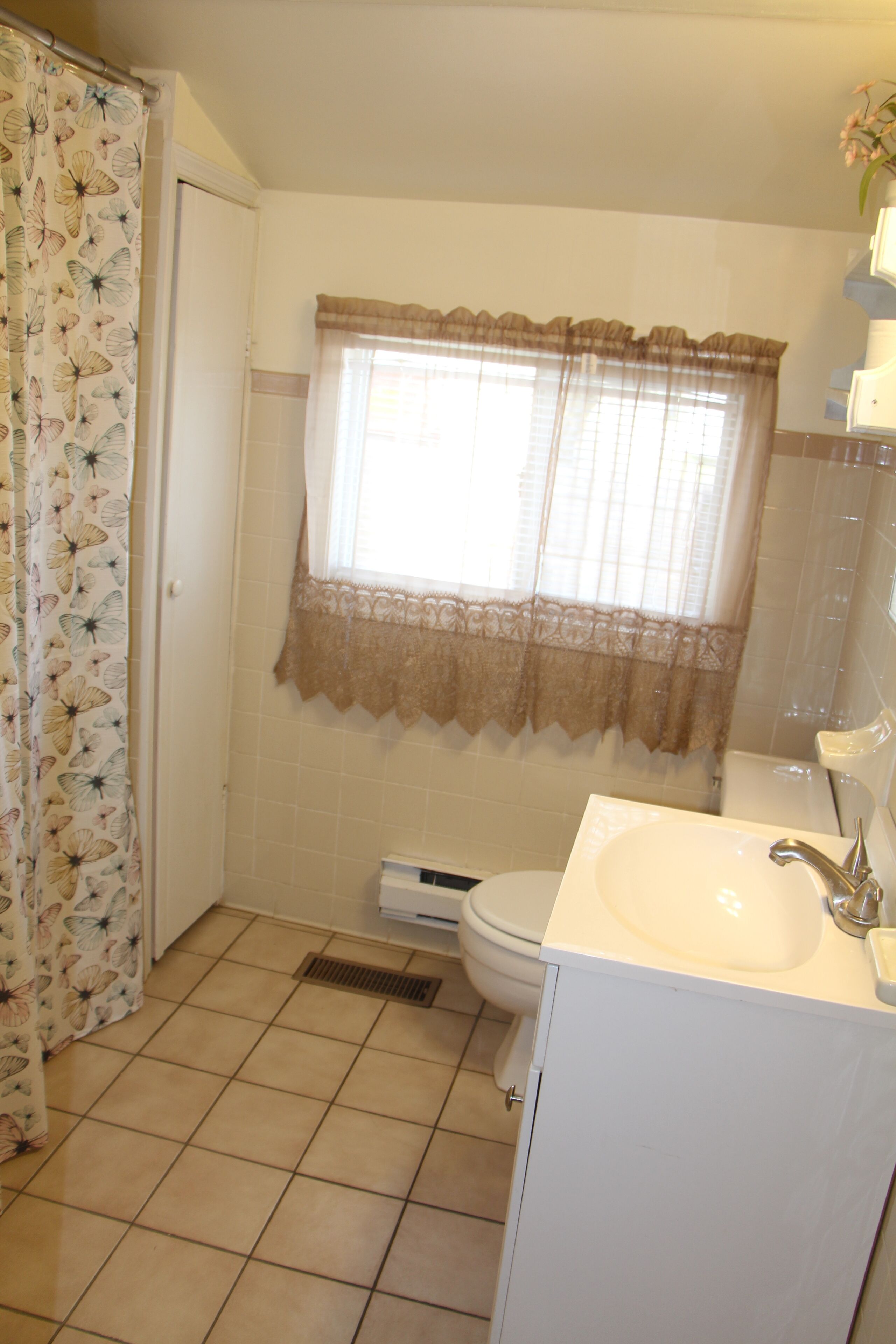 Une salle de bain avec des toilettes, un lavabo et une fenêtre ornée de rideaux en dentelle.