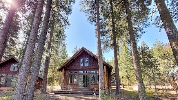 Una cabaña de madera con ventanas amplias, rodeada de árboles altos.