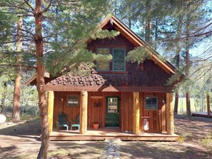 A rustic cabin with a front porch, two windows, and a chimney.