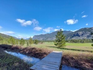 A wooden dock extending into a body of water, surrounded by a grassy field and a mountainous landscape. - Aspen Lodge at Timberline Meadows, 1st Floor Unit (Winthrop)