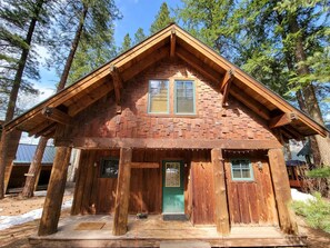 A rustic cabin with a steeply pitched roof, wooden exterior, and a front porch.
