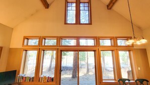 A room with large windows, a dining table set for two, and a bookshelf with books. - Crazy Squirrels Cabin at Timberline Meadows (Winthrop)