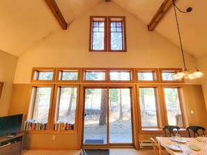 Ein Zimmer mit großen Fenstern, einem für zwei Personen gedeckten Esstisch und einem Bücherregal mit Büchern.