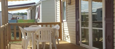 A covered outdoor deck with a wooden table and chairs, a pergola overhead, and a sliding glass door leading to a covered patio area.
