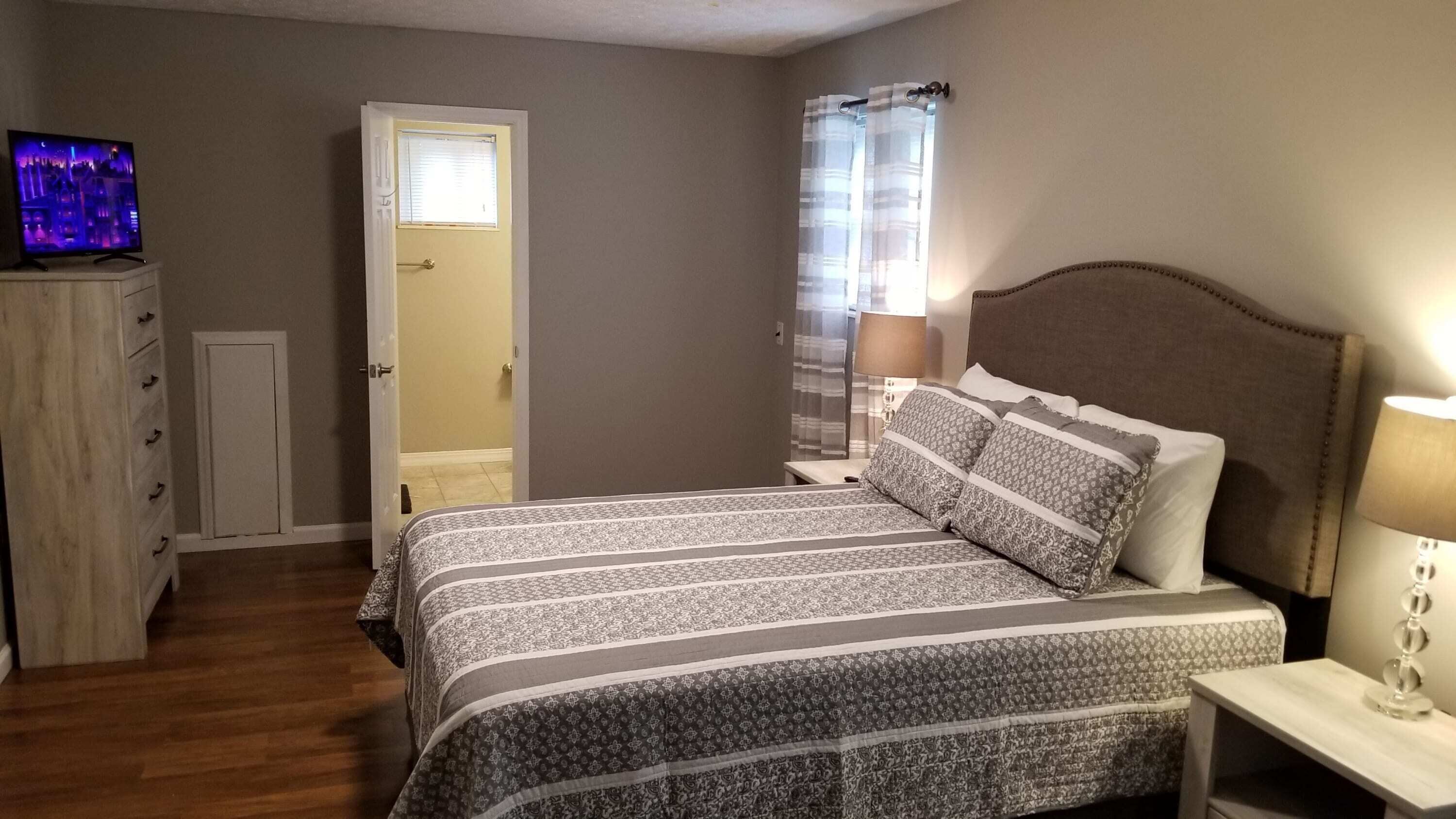 Une chambre à coucher comprenant un lit, une table de chevet, un téléviseur et une porte donnant sur une autre pièce.