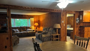 A cozy cabin interior with a wooden dining table, two sofas, and a ceiling fan.