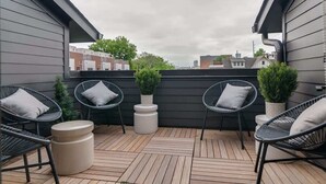 En tagterrasse med fire sorte fletstole, hver med hynde, og to små krukker med planter.