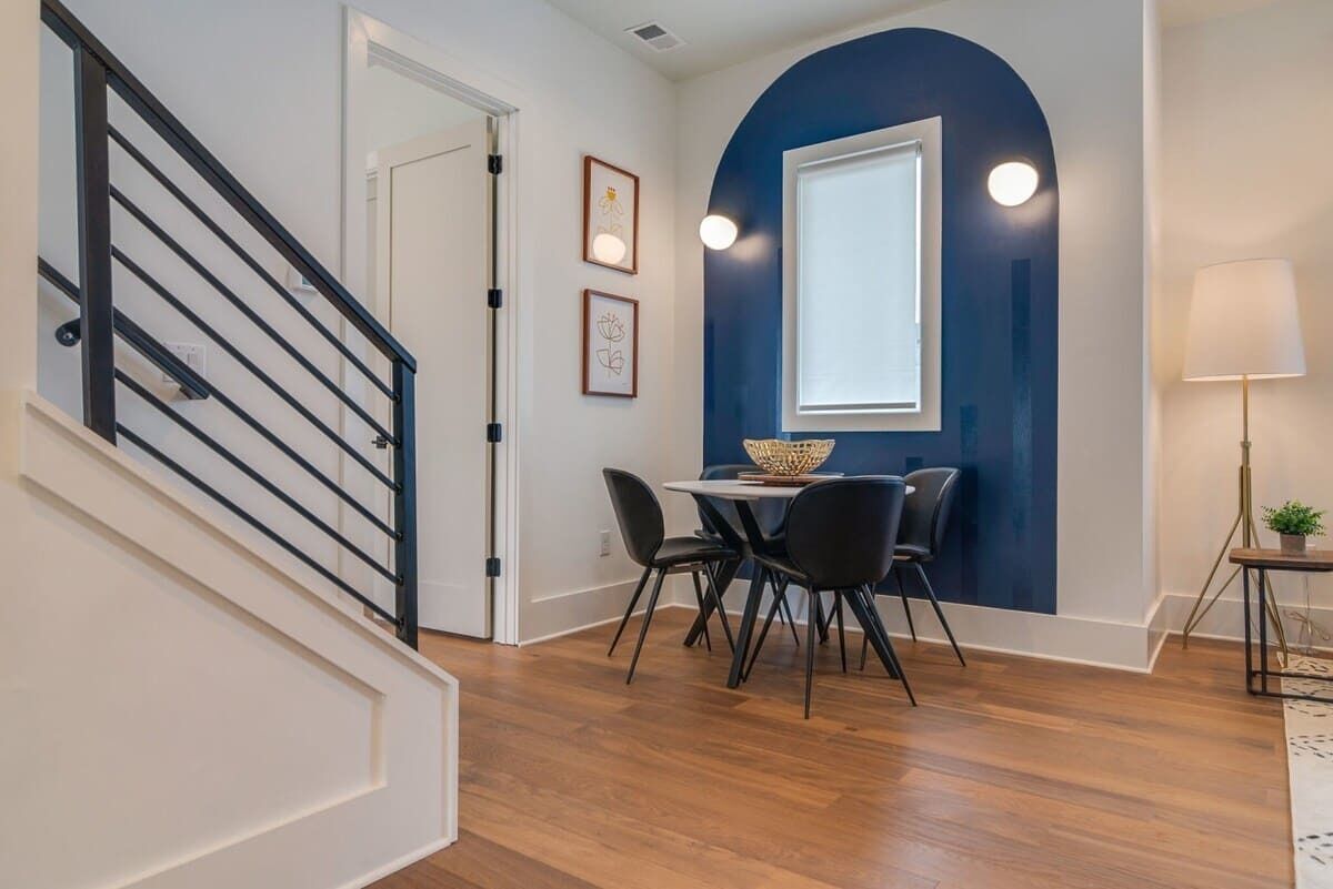 Un intérieur moderne avec un escalier, un coin repas comprenant une table ronde et des chaises, et une grande fenêtre offrant une vue dégagée.