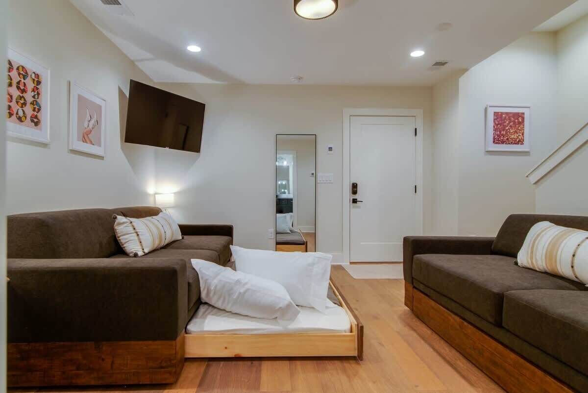 A modern living room with two sofas, a wooden bed frame, and a flat-screen TV mounted on the wall.
