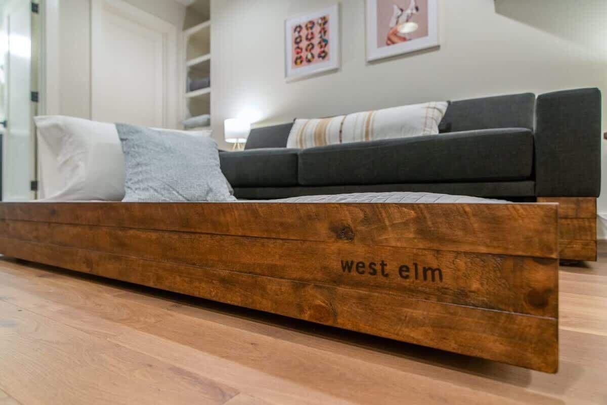 A modern living room with a wooden bed labeled 'west elm' and a grey sofa.