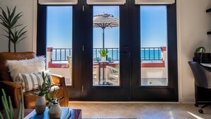 Un salón con vistas al océano a través de un ventanal, un sofá de cuero marrón, una mesa de centro con libros y plantas, y una alfombra estampada.