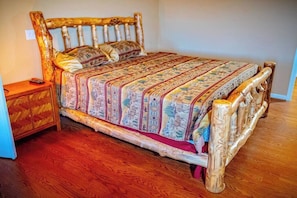 Una cama de madera con colcha y almohadas estampadas, una mesita de noche con cajón y suelo de madera.