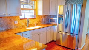 A kitchen with white cabinets, a stainless steel refrigerator, a microwave, and a window with blinds. - Royal Ranch (Cañon City)