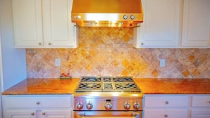 Una cocina con gabinetes blancos, una campana extractora de acero inoxidable, una estufa a gas y un horno empotrado.