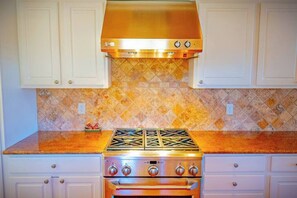 A kitchen with white cabinets, a stainless steel range hood, a gas stove, and a built-in oven. - Royal Ranch (Cañon City)