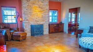 A spacious living area with a stone wall, a piano, a sofa, and a patterned ottoman. - Royal Ranch (Cañon City)