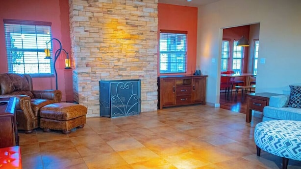 Amplia sala de estar con pared de piedra, un piano, un sofá y un otomano estampado.