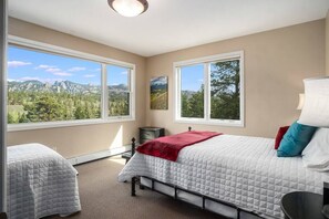 Un dormitorio con dos camas, ventanas amplias y vistas a montañas.