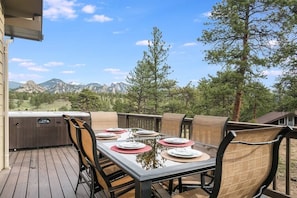 Un área de comedor al aire libre con una mesa lista para cuatro personas, rodeada de sillas, con vistas a un paisaje montañoso.
