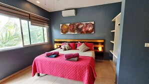 Un dormitorio con cama, cabecera, mesita de noche, aire acondicionado de pared y ventana con persianas.