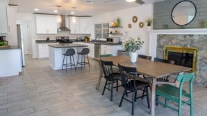 A modern kitchen with white cabinets, a central island, and a dining area with a wooden table and chairs. - Prickly Pear Desert Oasis- 3 Bedroom/Pool/Spa/Putting Green (Glendale)