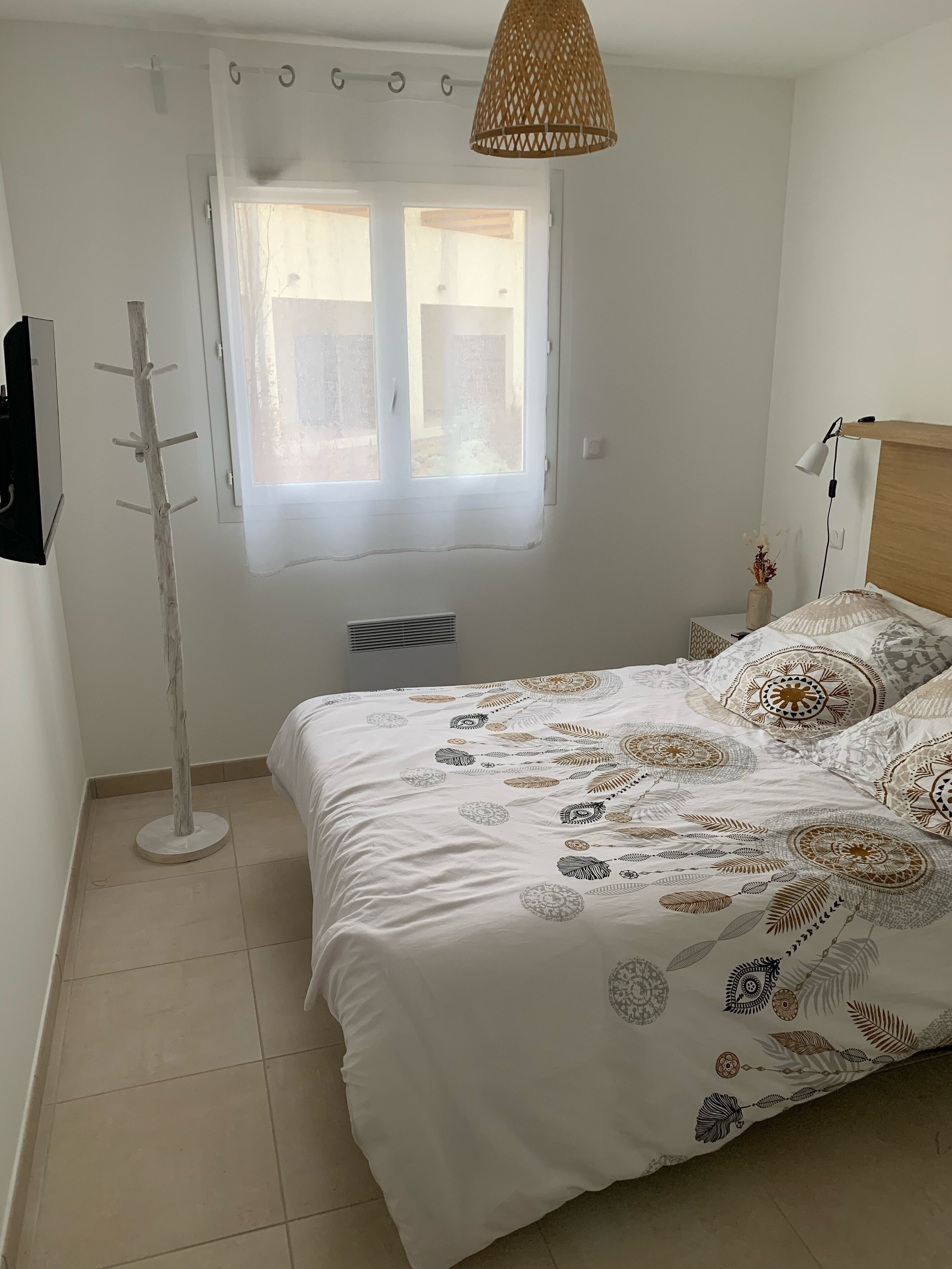 A bedroom with a bed, a window, a standing lamp, and a coat rack.