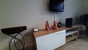 Een woonkamer met een flatscreen televisie aan de muur, een houten salontafel, een witte kast met een lade en een kleine kerstboomversiering.