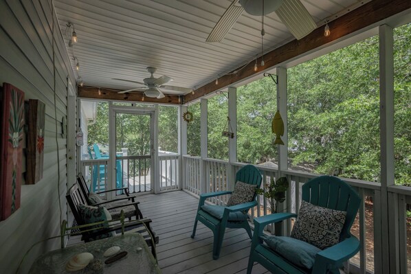 A covered porch with two chairs, a table, and a ceiling fan.