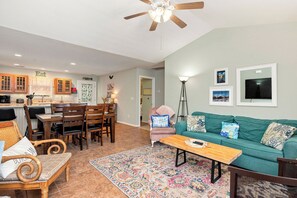 A well-lit living room with a green sofa, a coffee table, and a dining area with wooden chairs and a table.