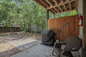 A covered patio area with a grill, a covered chair, and a wooden fence. - Fitz Us Fine: Spacious, Adorable Beach Home in Family-friendly Neighborhood (Oak Island)