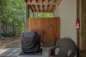 A covered outdoor area with a wooden door, a covered grill, and a fire extinguisher mounted on the wall.