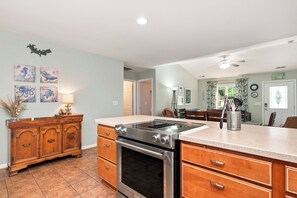 A kitchen with a stove, oven, and wooden cabinets. There are wall art pieces and a ceiling fan.