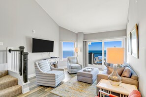 Relax in this spacious living room with a high ceiling, featuring a large flat-screen TV, comfortable seating area, and ocean views.